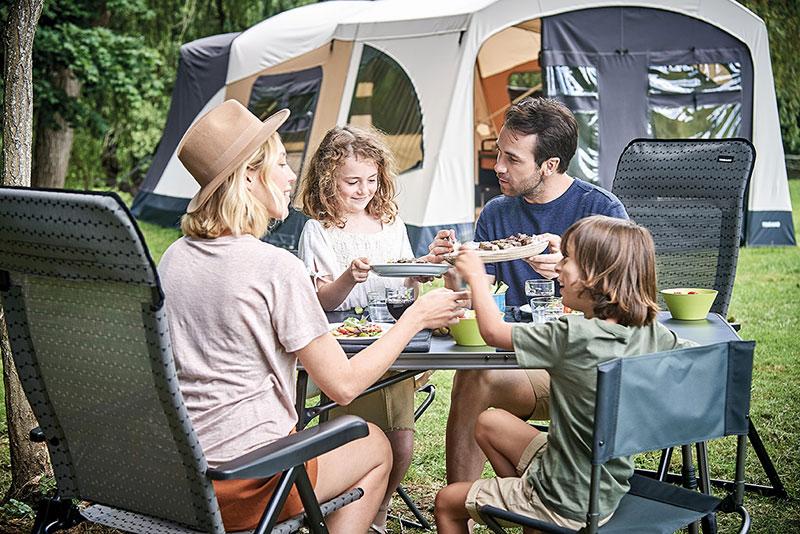 Une famille de quatre personnes est assise autour dune table de camping, en train de manger.
