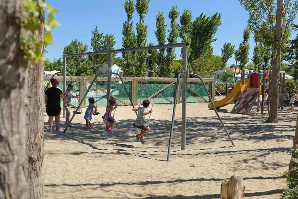 Une aire de jeux pour enfants avec des balançoires, un toboggan et un bac à sable.