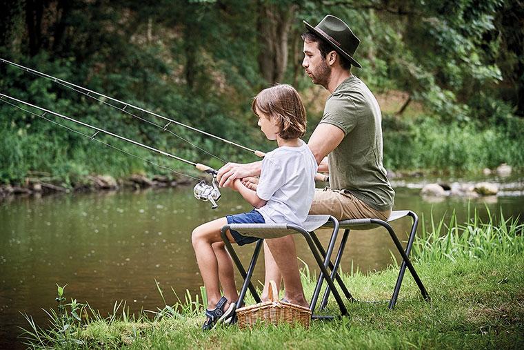 Un père et son fils sont assis sur des chaises pliantes et pêchent dans une rivière.