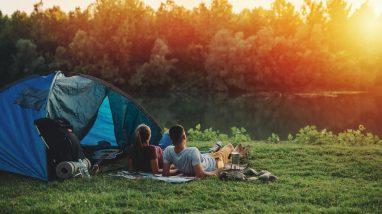 Un couple est allongé sur lherbe devant une tente au bord dune rivière.