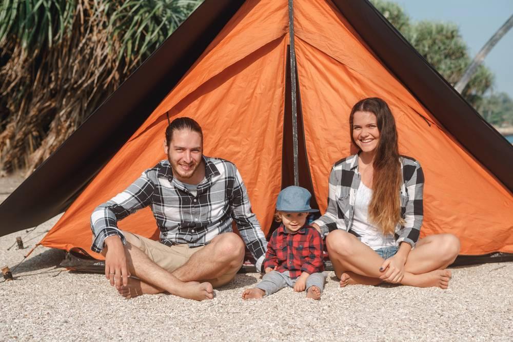Une famille de campeurs est assise devant sa tente sur la plage.