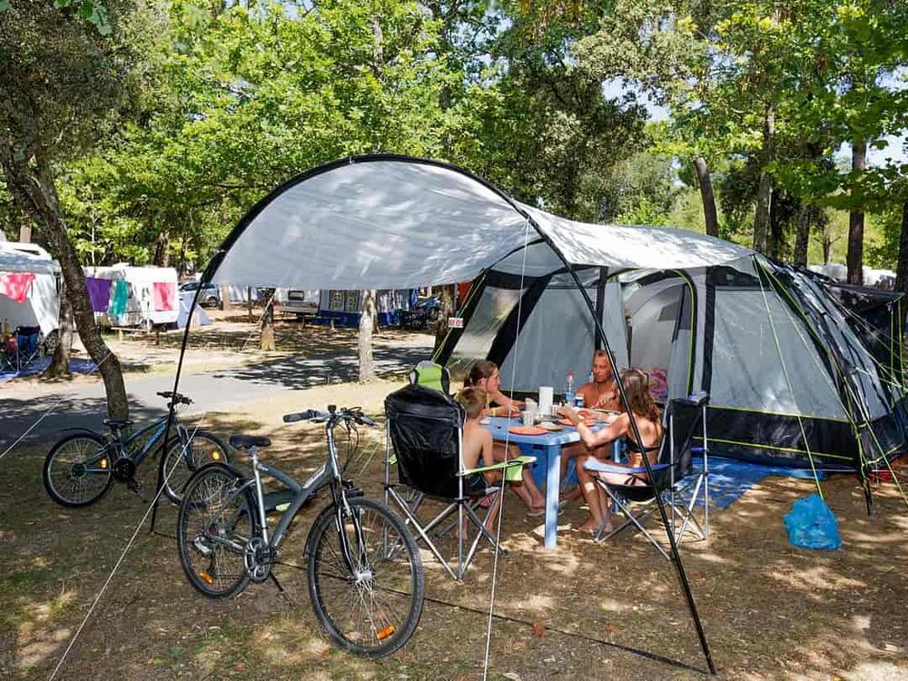 Une famille est en train de manger devant sa tente dans un camping.
