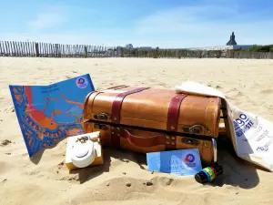Une valise marron ouverte sur la plage avec une carte, un appareil photo et dautres objets à côté.