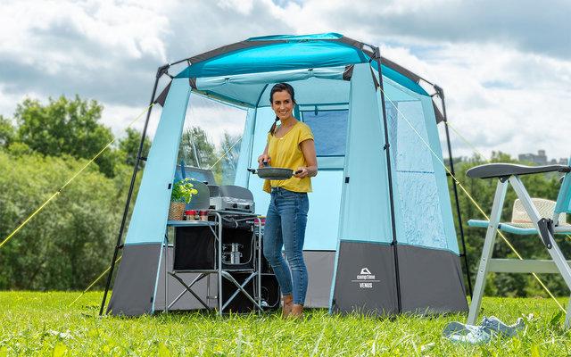 Une femme se tient dans une tente de camping et cuisine sur une cuisinière à gaz.