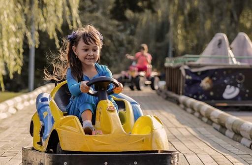 Une jeune fille souriante conduit un kart sur une piste en bois.