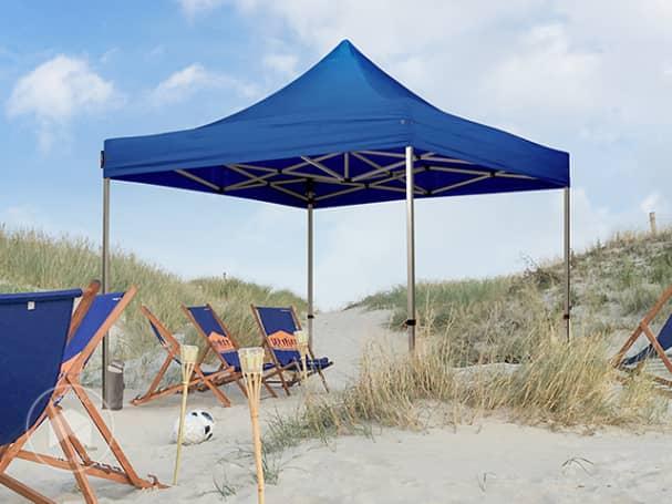 Une tente de plage bleue est installée sur le sable avec des chaises longues et des bouées à proximité.