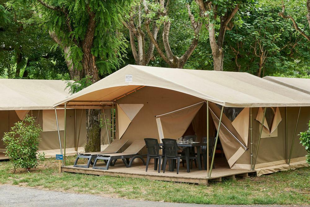 Une tente de safari avec une terrasse en bois, des chaises et des chaises longues devant.