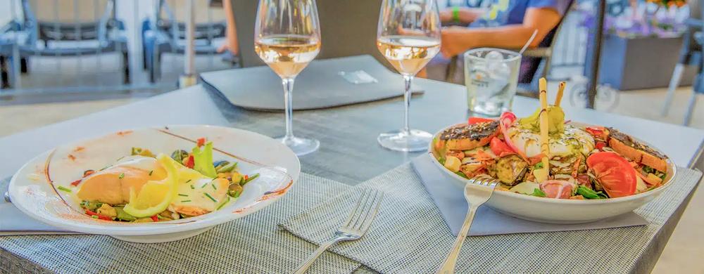 Une table de restaurant avec deux verres de vin, une assiette de poisson et une assiette de salade.
