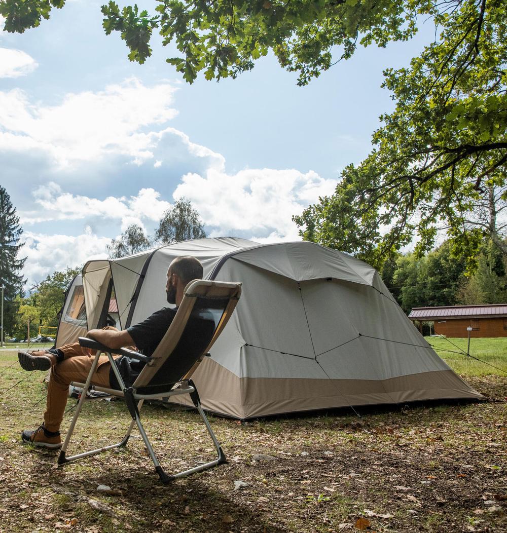 Un homme est assis sur une chaise de camping et regarde une tente.