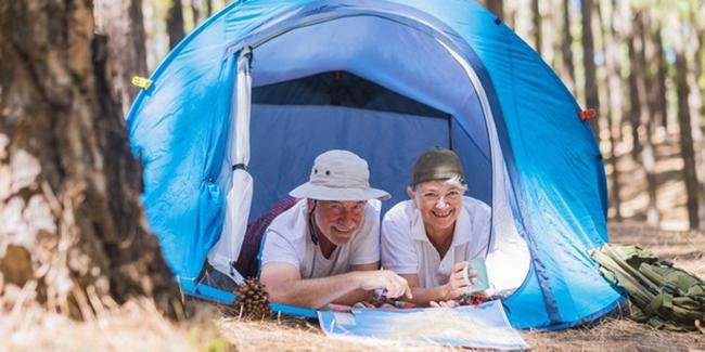 Un couple de personnes âgées est allongé dans une tente et regarde une carte.
