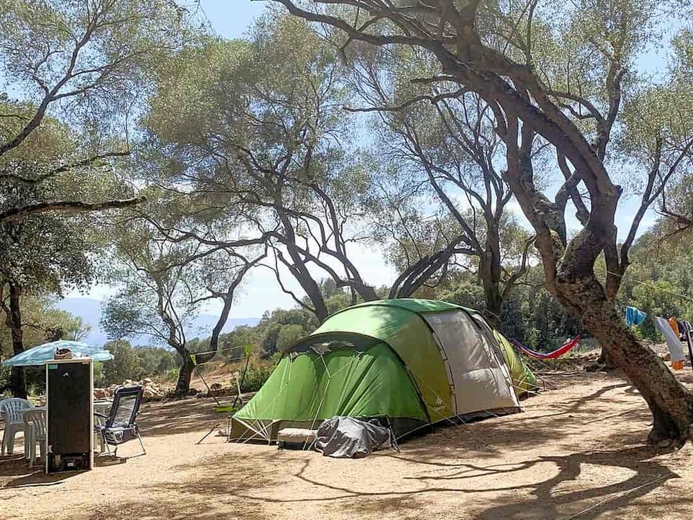 Une tente verte est installée sur un terrain de camping ombragé.
