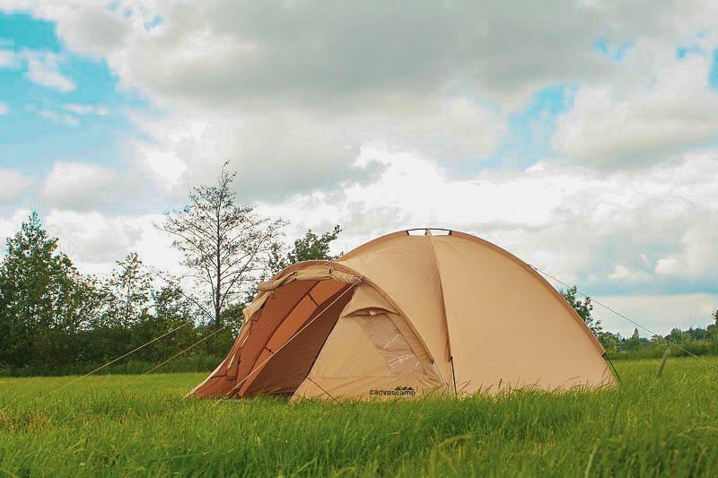 Une tente de camping beige est installée dans un champ verdoyant.