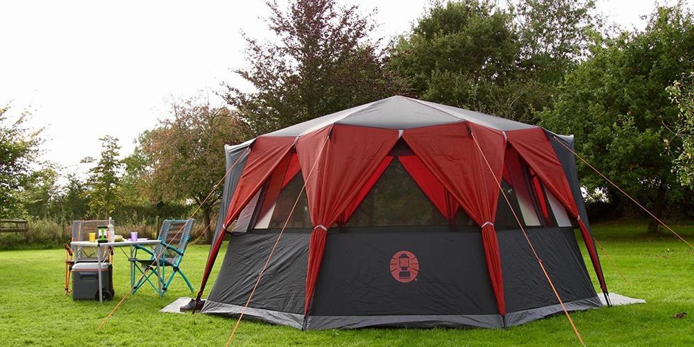 Une tente de camping rouge et noire est installée dans un champ.