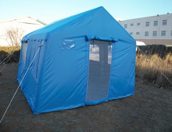 Une tente de secours bleue est montée sur un terrain vague.