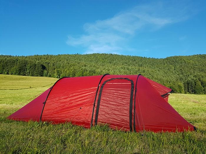 Une tente rouge est installée dans un champ avec des arbres en arrière-plan.