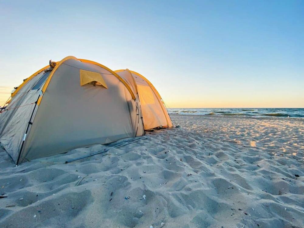 Une tente de camping beige est installée sur une plage de sable fin au bord de la mer.