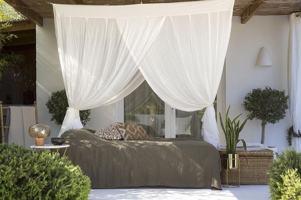 Une moustiquaire blanche entoure un lit de repos vert placé sur une terrasse.