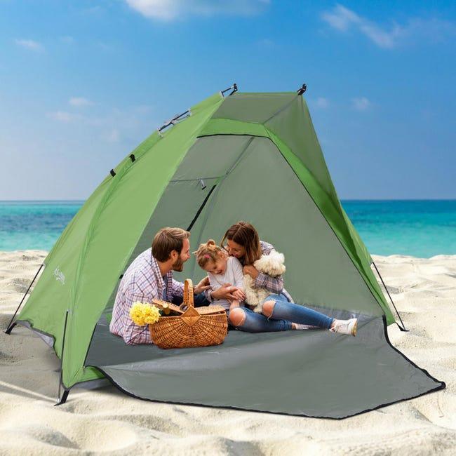 Une famille heureuse est assise dans une tente de plage verte sur le sable.