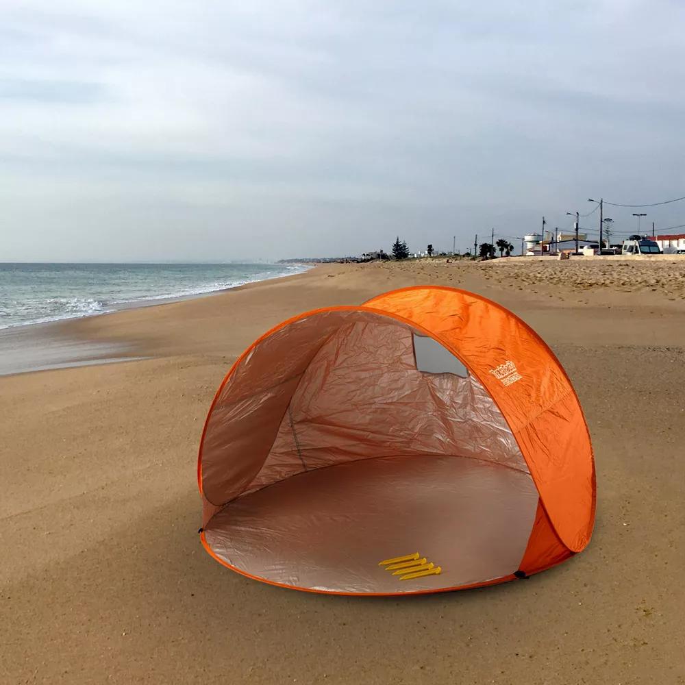 Une tente de plage orange est installée sur le sable avec la mer en arrière-plan.