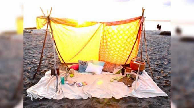 Une tente de plage avec des draps jaunes et blancs, des oreillers et des couvertures sur le sable.
