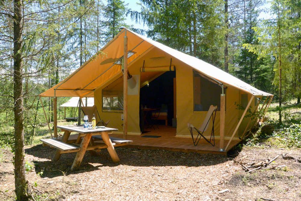Une tente de safari spacieuse et confortable avec une terrasse et un coin salon, située dans une forêt.