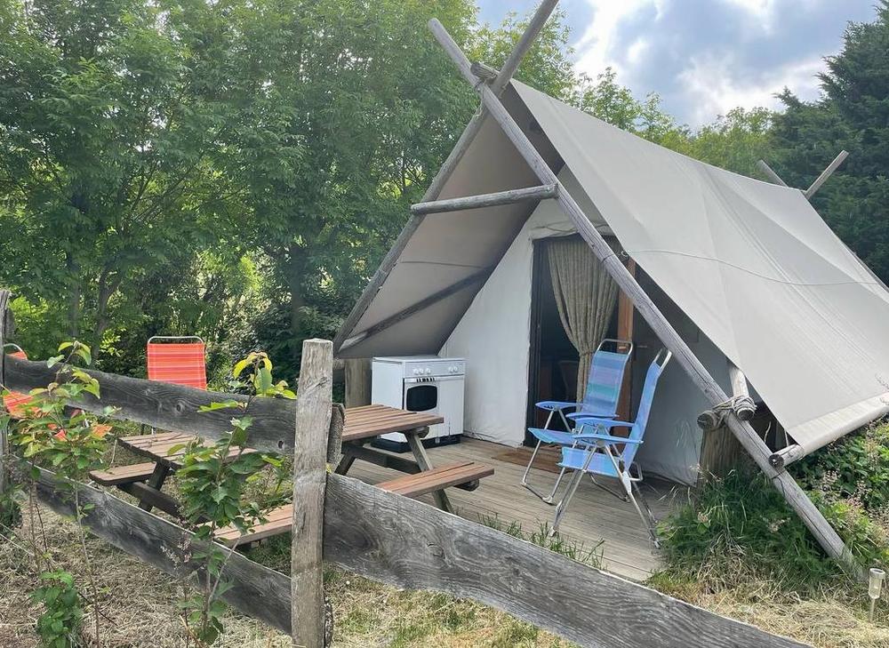 Une tente de safari avec une terrasse, des chaises et une table de pique-nique.